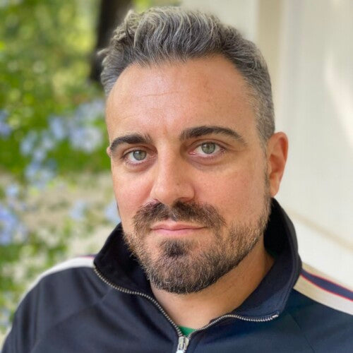 Robert Bryndza with gray hair and beard wearing a dark jacket outdoors